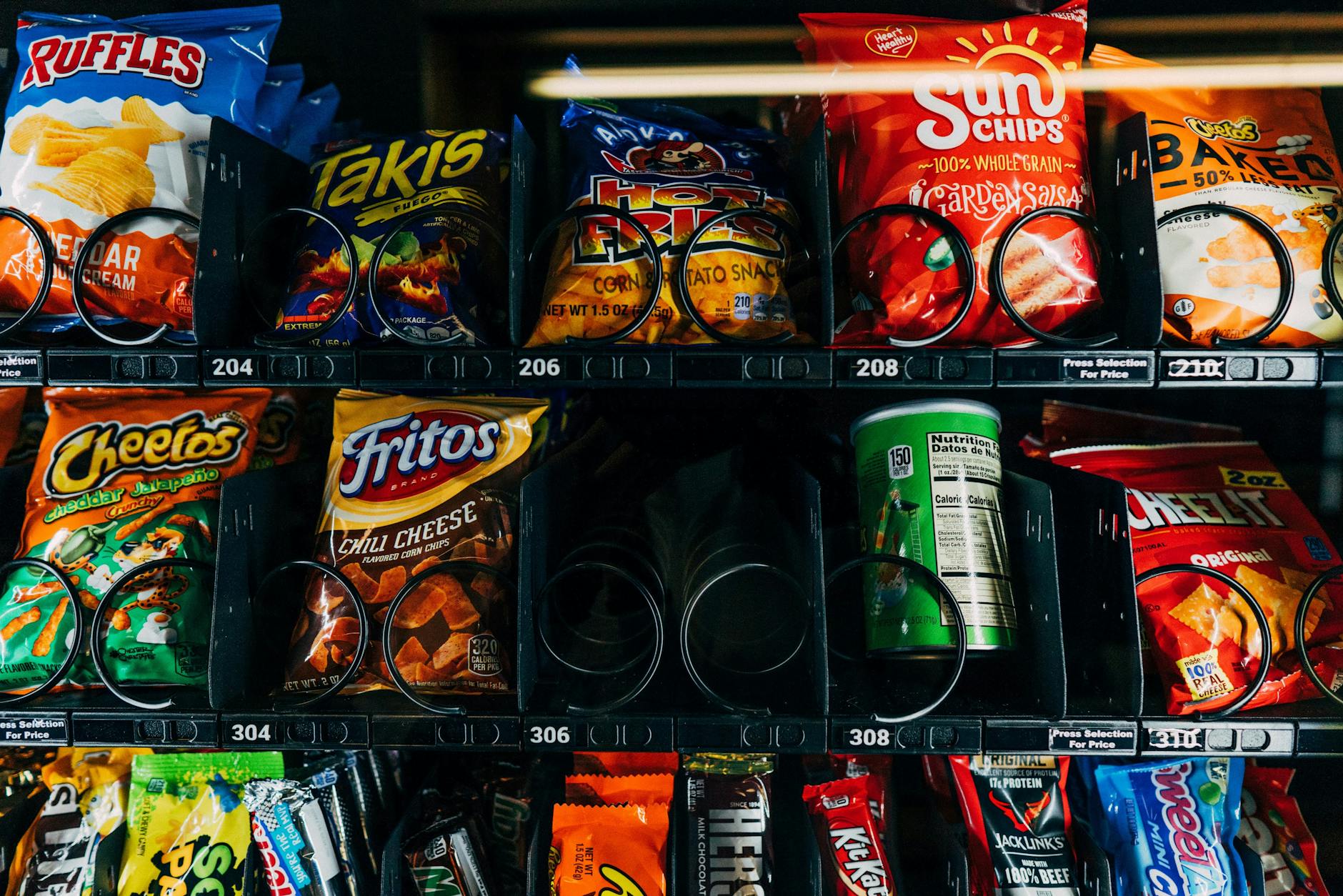 A vending machine displaying a variety of snack options including chips, Cheetos, Fritos, and Sun Chips.